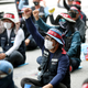 A group of sitting people in hats and face masks lift their fists.